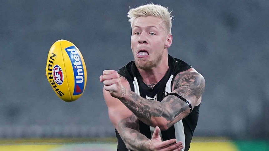 A Collingwood AFL player handballs with his left hand during a night match against Richmond at the MCG in Melbourne.