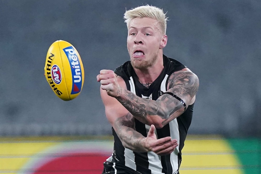A Collingwood AFL player handballs with his left hand during a night match against Richmond at the MCG in Melbourne.