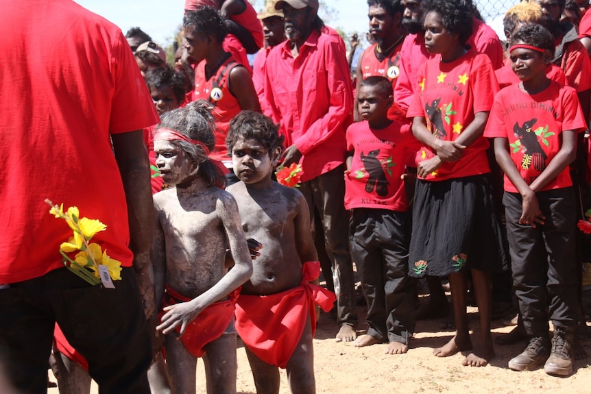 Young children in body paint stand with a crowd wearing red.
