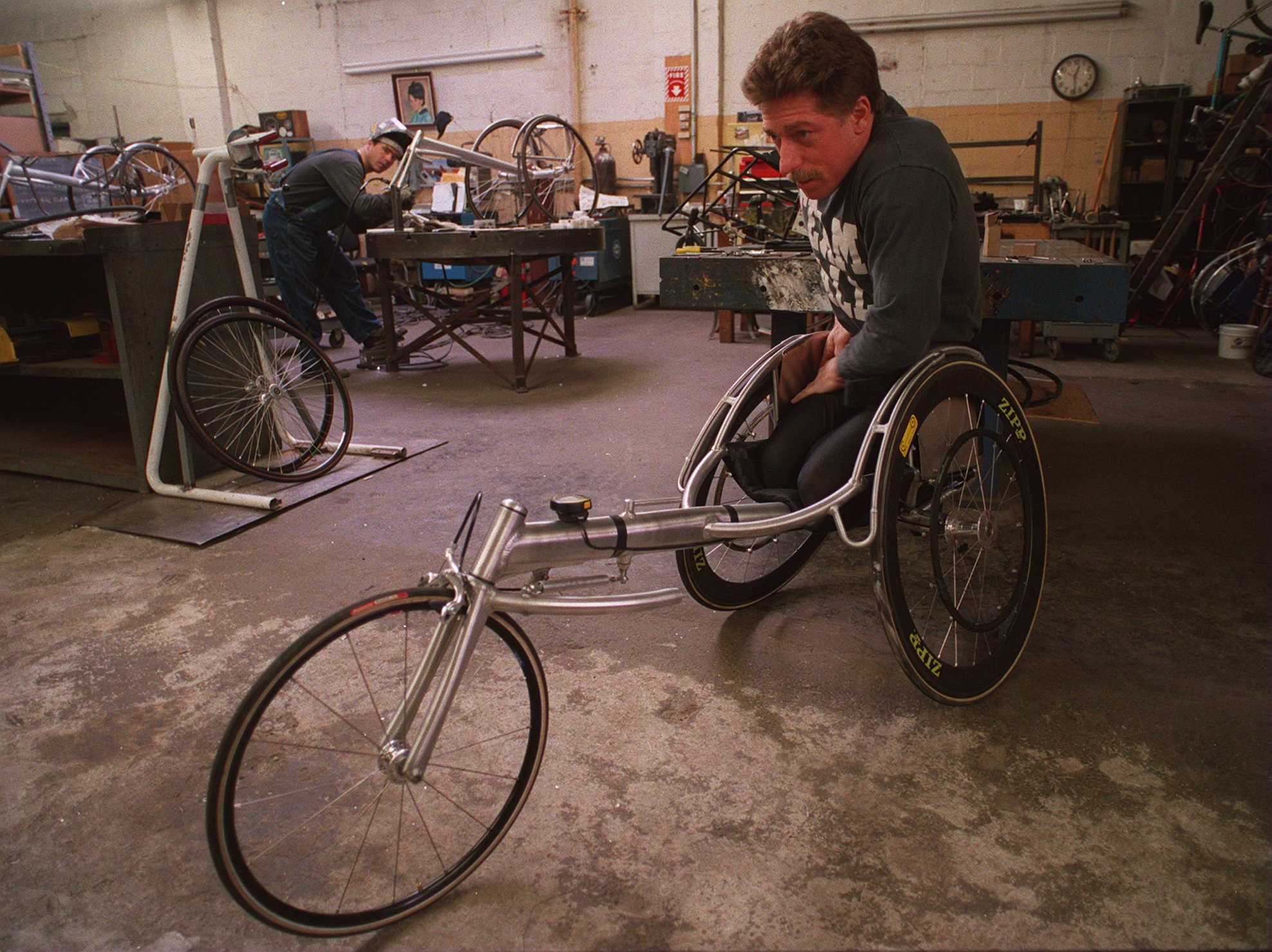 Uma foto de um jovem Bob Hall na oficina, sentado em uma cadeira de três rodas projetada para corridas.