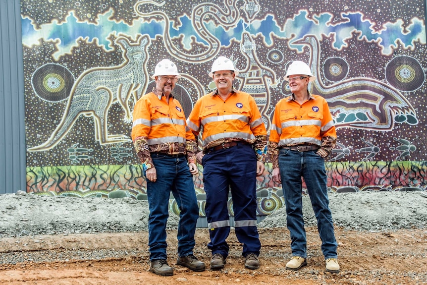 Men in hi-vis stand in front of Aboriginal artwork at the Nova Nickel Mine in Western Australia.