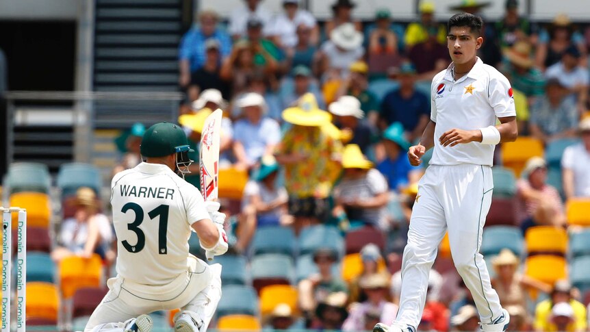 Pakistan bowler Naseem Shah stands over a crouching David Warner during a Test.