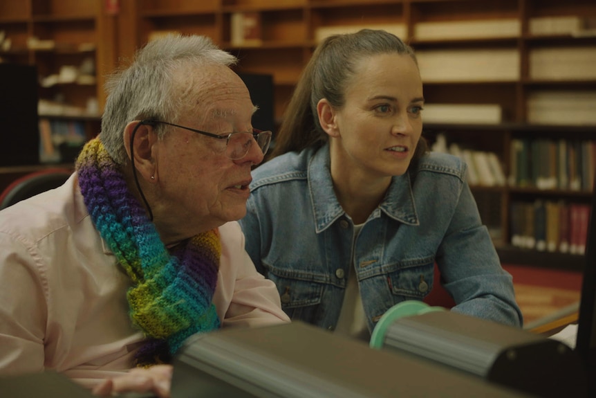 Elderly man and woman looking at screen in a library.