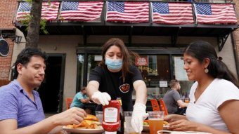 Two Americans eat at a restaurant while their waiter wears a mask.