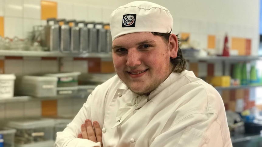A young man wearing a chef's outfit in a kitchen.