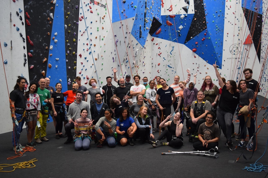Around 30 people gather smiling for a group photo in a climbing hall.
