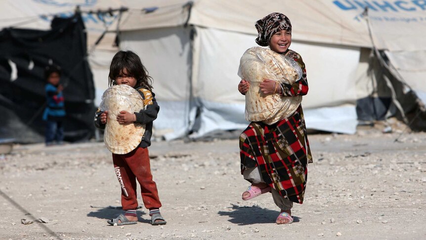 Two little girls carrying flat breads past UNHCR tents