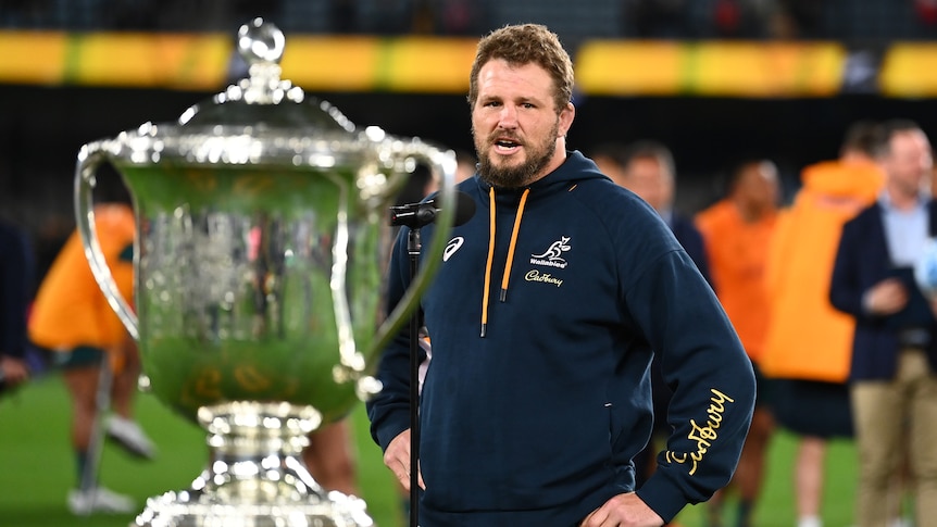 Wallabies captain James Slipper in a tracksuit looks at the Bledisloe Cup in the foreground after the match.