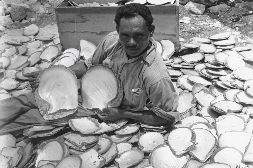 A man sitting on ground surrounded by pearl shells