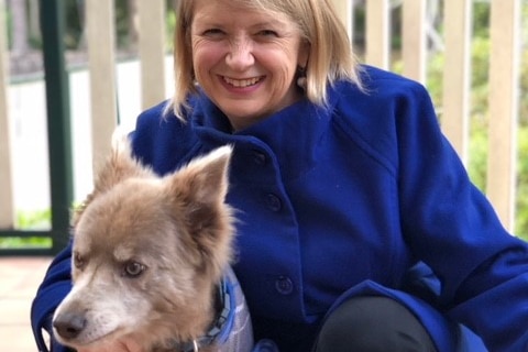 A woman kneeling and smiling with her arm around a grey dog to depict stories of how dogs get people through tough times.