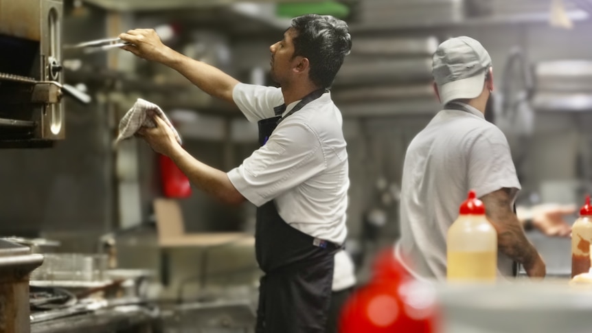 Kitchen worker uses tongs in a pub kitchen in Sydney.