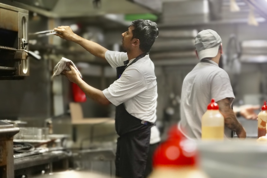 Kitchen worker uses tongs in a pub kitchen in Sydney.