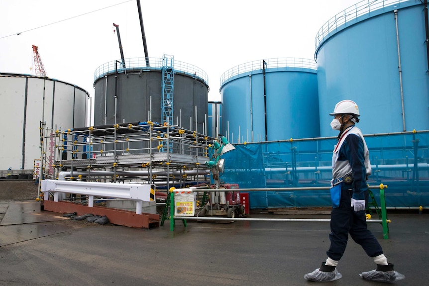 Un angajat trece pe lângă rezervoare uriașe de stocare a apei contaminate de culoare albă, albastră și neagră de la uzina Fukushima.