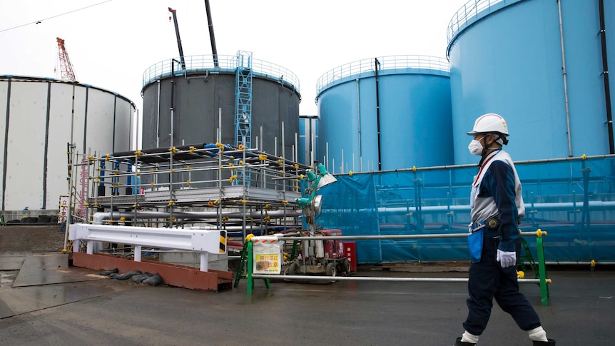 An employee walks past huge white, blue and black storage tanks for contaminated water at the Fukushima plant.