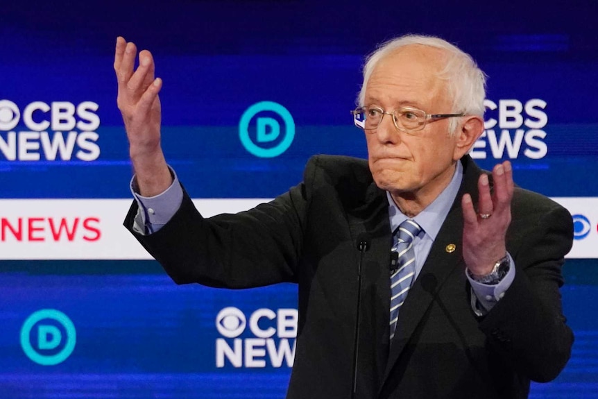 Elizabeth Warren and Bernie Sanders speak on a stage during the democratic primary.