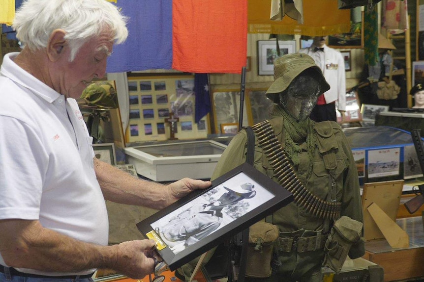 A man looks at a framed black and white photo of a soldier