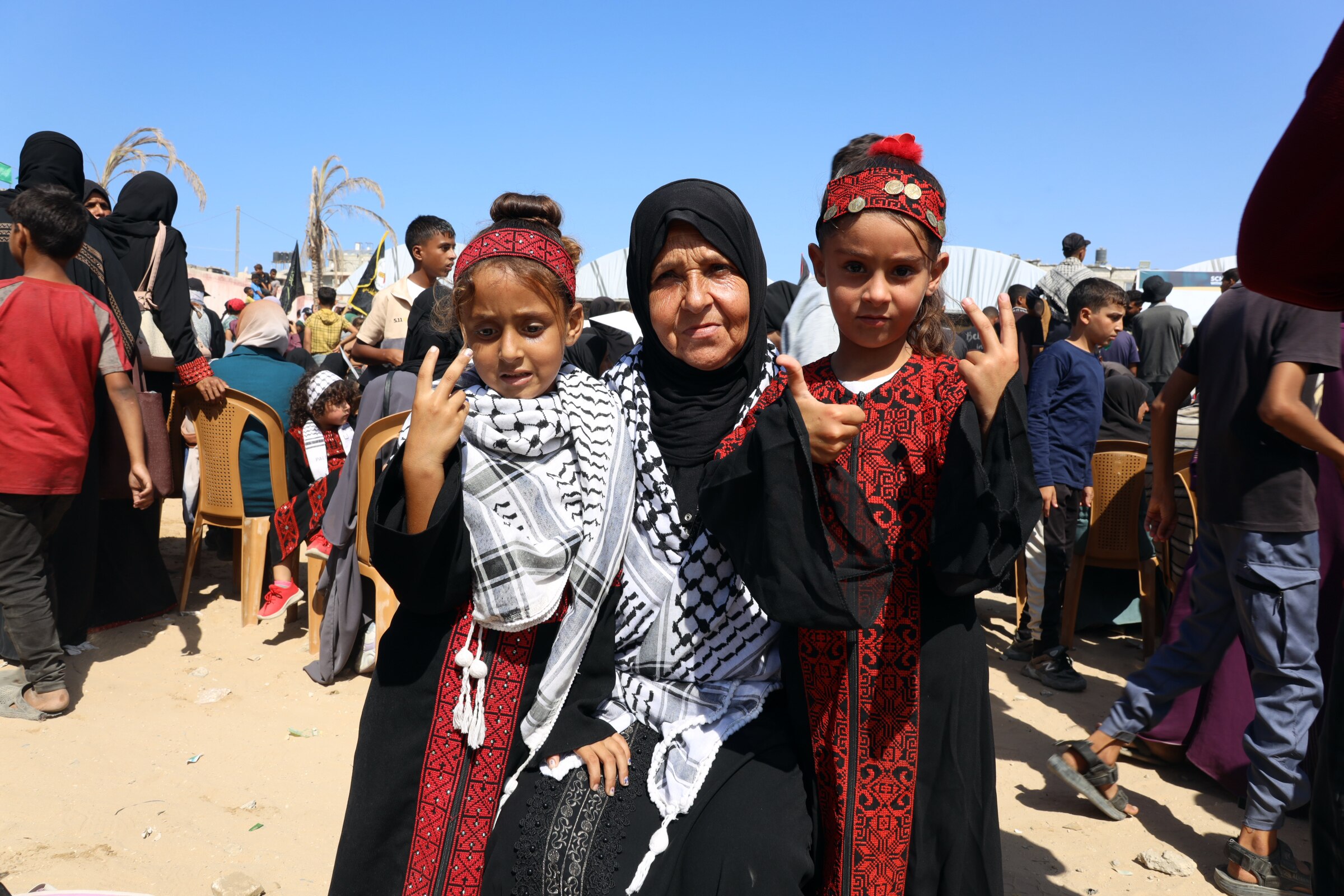 A Palestinian woman dressed in traditional dress puts her arms around two girls in Gaza.