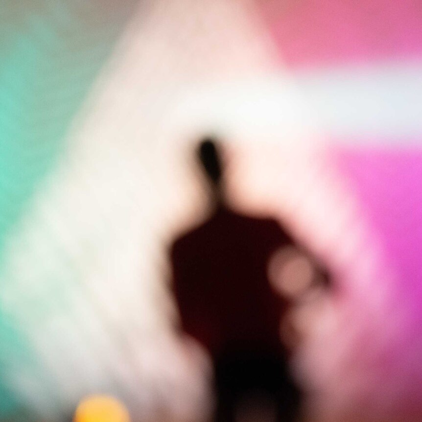 A blurred out silhouette if a man walking into bright blue and pink lights