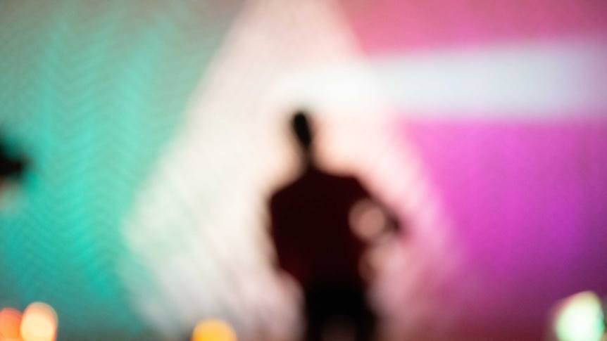 A blurred out silhouette if a man walking into bright blue and pink lights