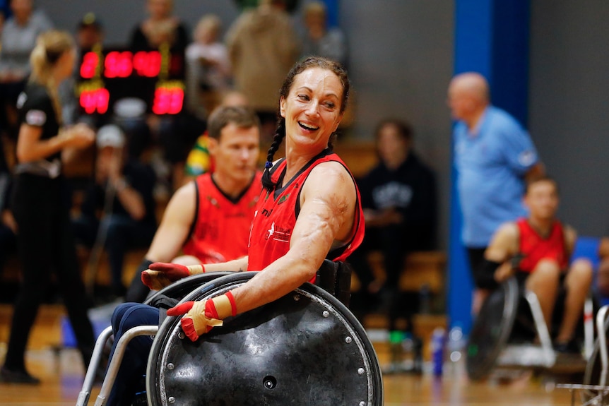 A woman in a wheelchair is smiling, while playing wheelchair rugby.