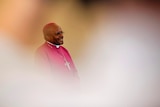 Archbishop Desmond Tutu is seen through crowds wearing dark pink religious robes.