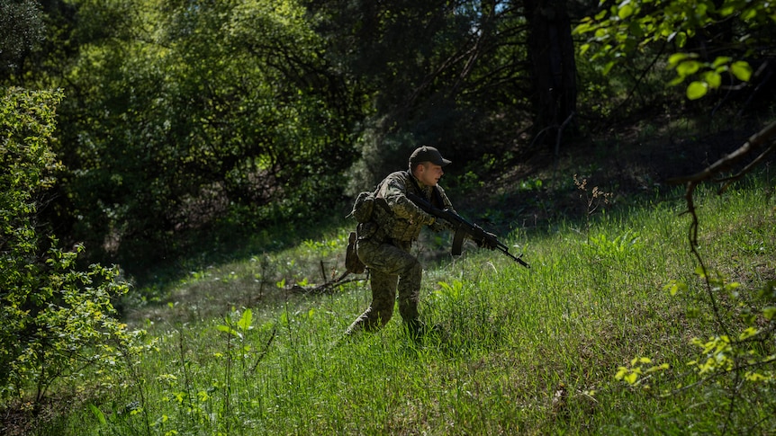 A soldier in uniform with a rifle walks up a grassy hill in Ukraine