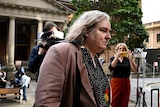 A transgender woman walks past photographs outside a court house.