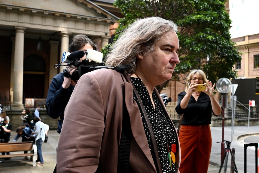 A transgender woman walks past photographs outside a court house.