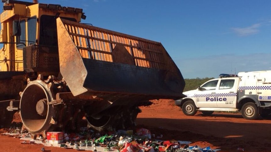 A large truck drives over a pile of alcohol while police watch on