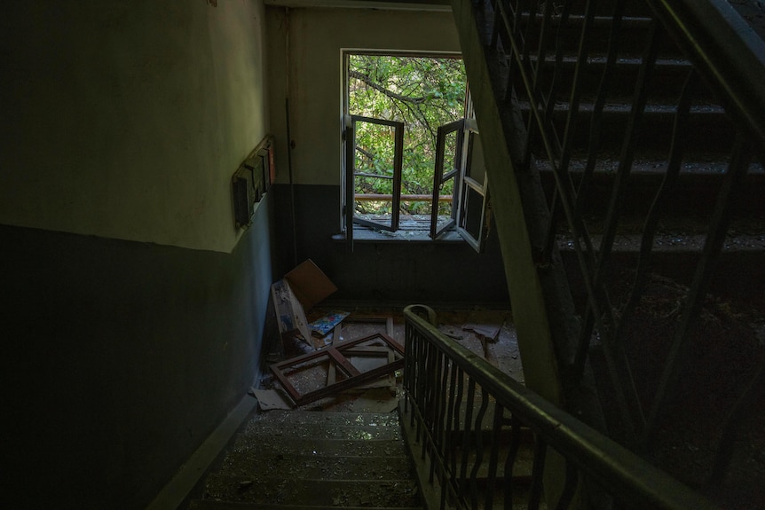 Looking down flight of stairs towards open window. Glass, damanged window shutters and other debris on the landing.
