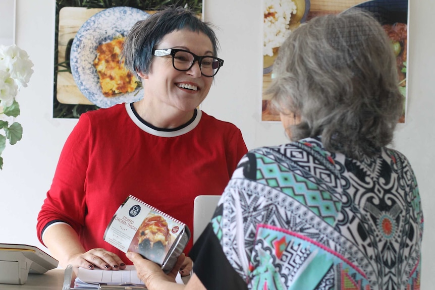 Karen MacDonald serving a customer with posters on the walls behind showing the food the shop sells