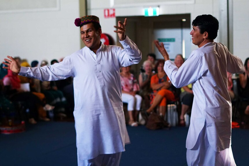 Two men in traditional dress dancing while a crowd applauds.