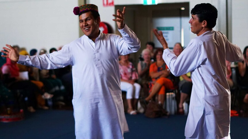 Two men in traditional dress dancing while a crowd applauds.