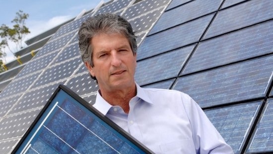 Professor Martin Green standing in front of a solar-panelled roof holding a solar panel