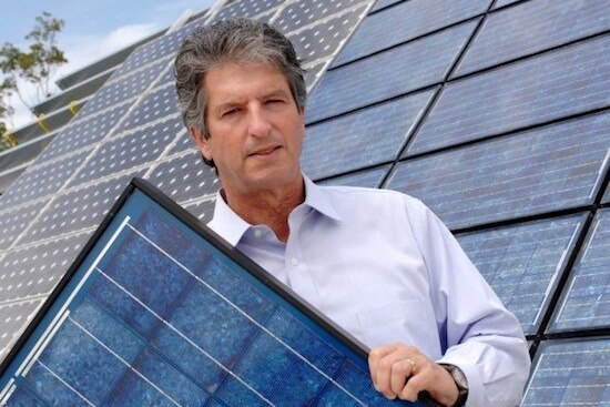 Professor Martin Green standing in front of a solar-panelled roof holding a solar panel