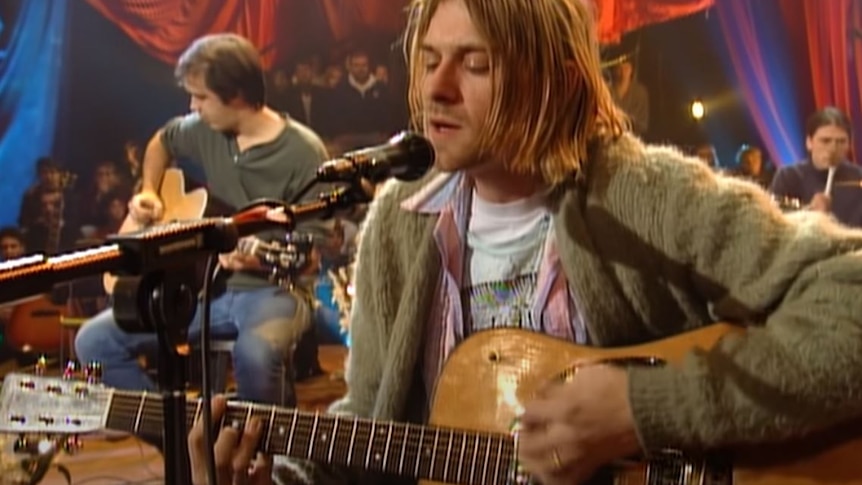 Kurt Cobain playing an acoustic guitar on stage.