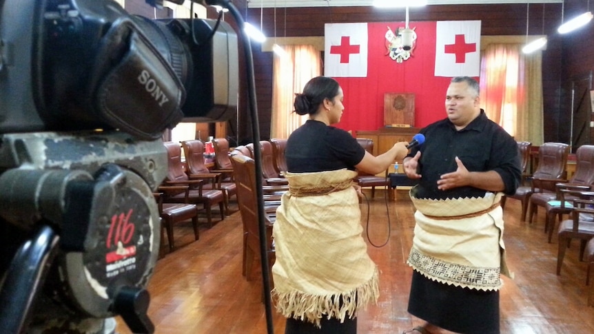 woman interviewing man in Tongan traditional dress with camera in foreground