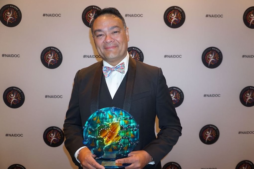 Kelvin Kong standing with an award. 