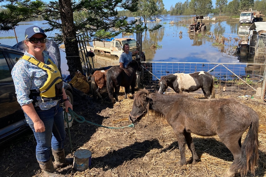 A woman in a blue shirt and yellow lifejacket stands with a miniature horse on a lead.