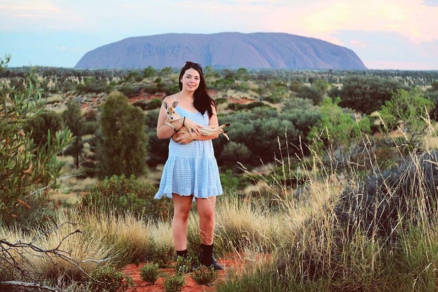 Australian traveller Amanda McDonald holds a kangaroo in front of Uluru.