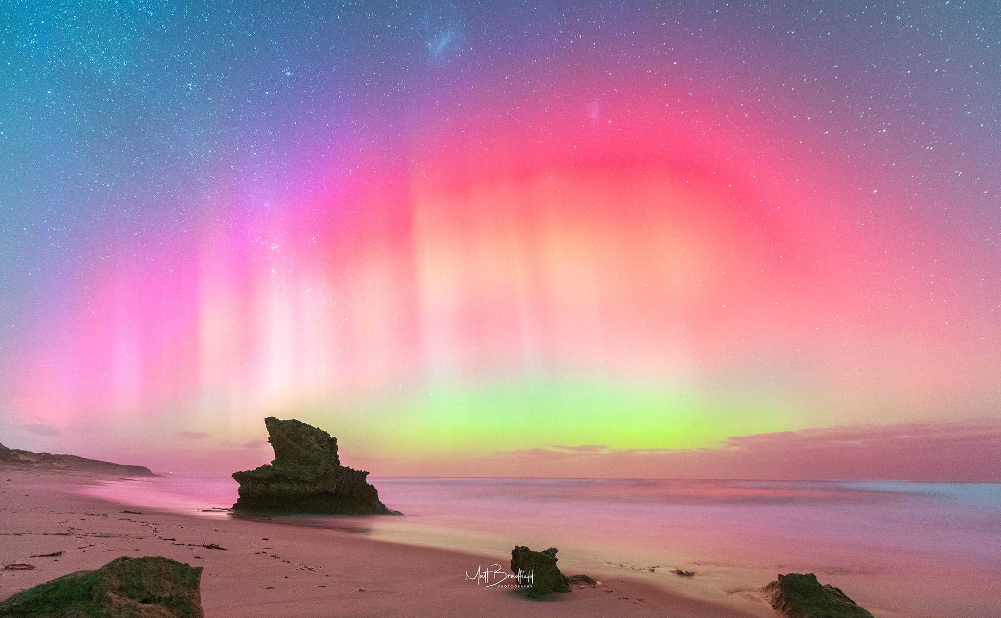 A pink and yellow hue aurora in the night sky by the beach