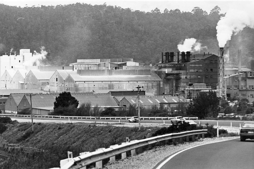 Tioxide factory, billowing smoke, viewed past cars travelling on Bass highway