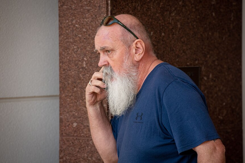 A white man with a silver beard exits court while on the phone