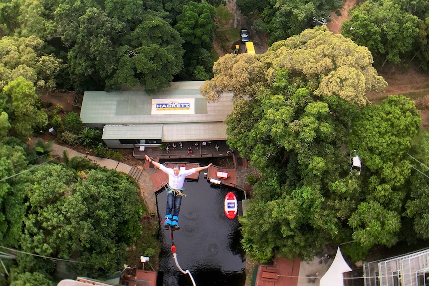 Overhead photo of man bungy jumping with AJ Hackett sign on roof of building.