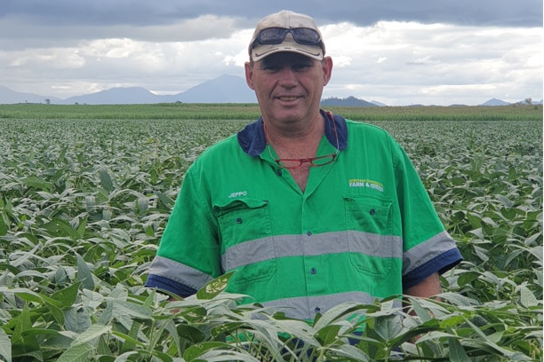 a man in a work shirt stands in a field smiling at the camera