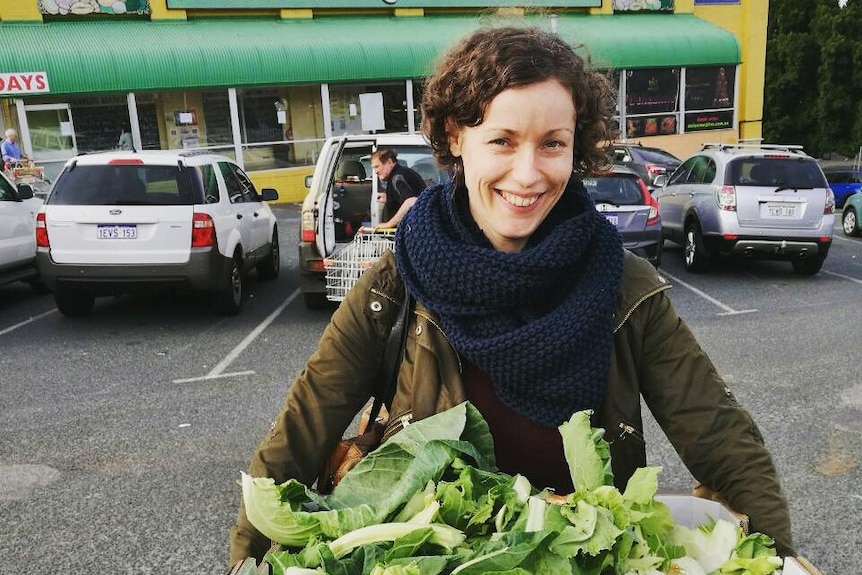 Lindsay Miles carrying a cardboard box with vegetables in it.