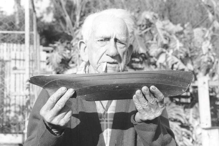 A black and white image of an old man holding a boat model with a cigarette in his mouth