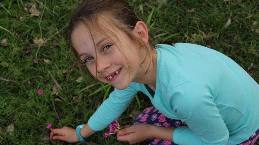 A young girl picks a flower.