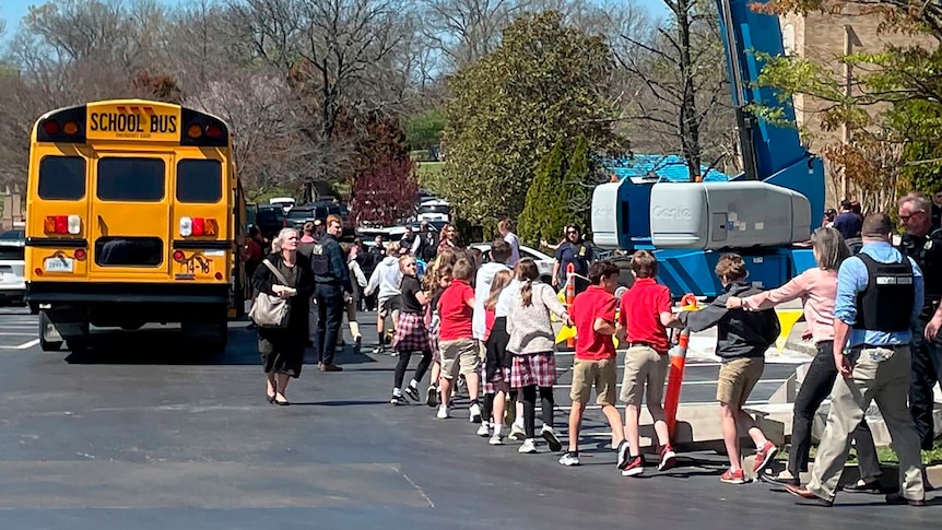 Teachers lead a row of children out of a school into an outdoor evacuation area