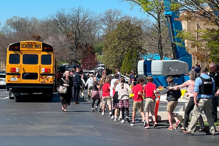 Teachers lead a row of children out of a school into an outdoor evacuation area